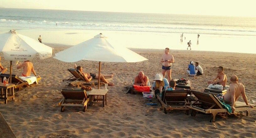Travelers relaxing on Batu Belig Beach under umbrellas at sunset, a popular hangout spot for gay-friendly tourism in Bali