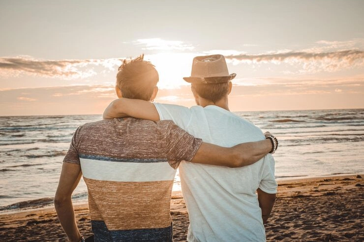 Two men embracing while watching the sunset on a beach, symbolizing romance, travel, and LGBTQ+ friendly experience