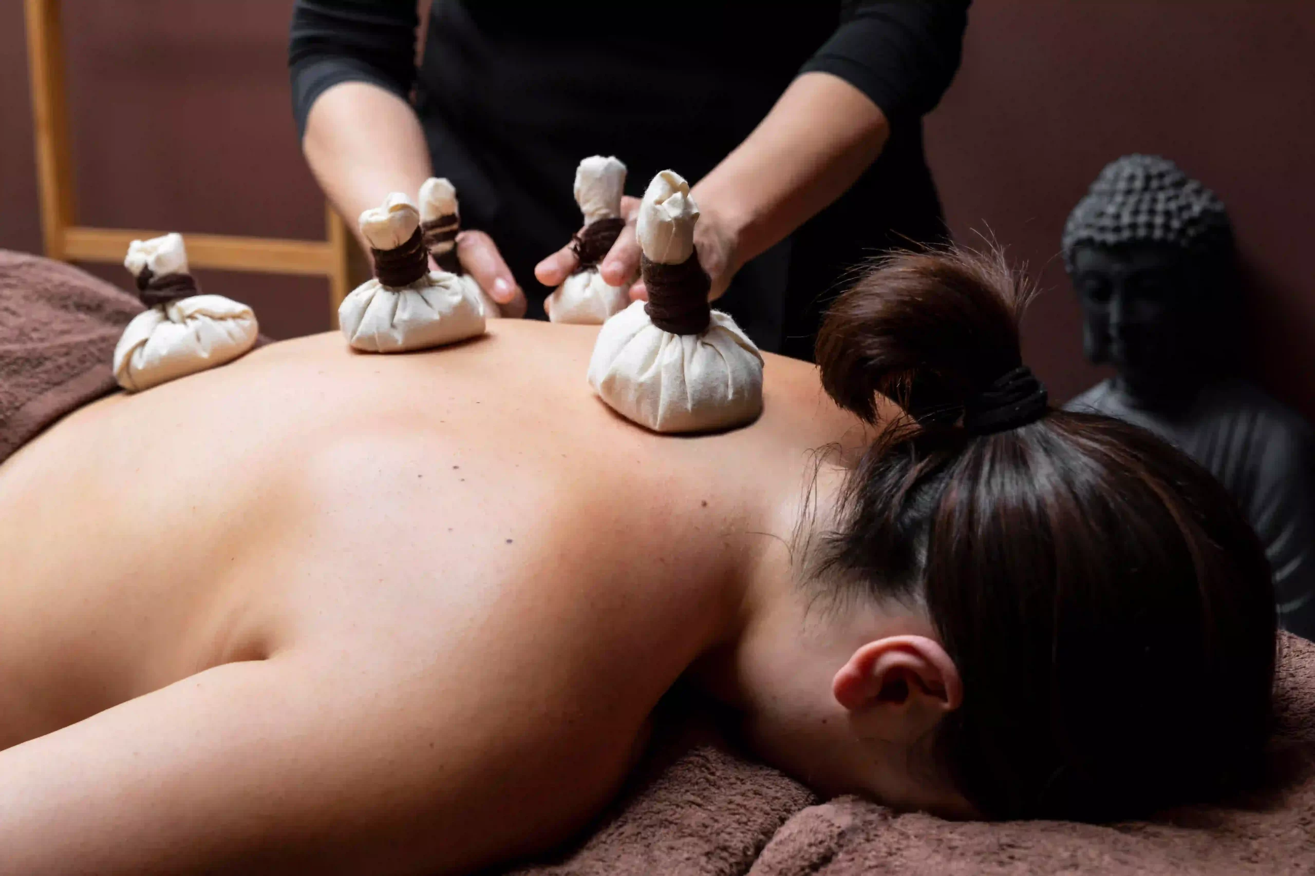 Close-up of a client receiving a back massage using multiple herbal poultice compresse