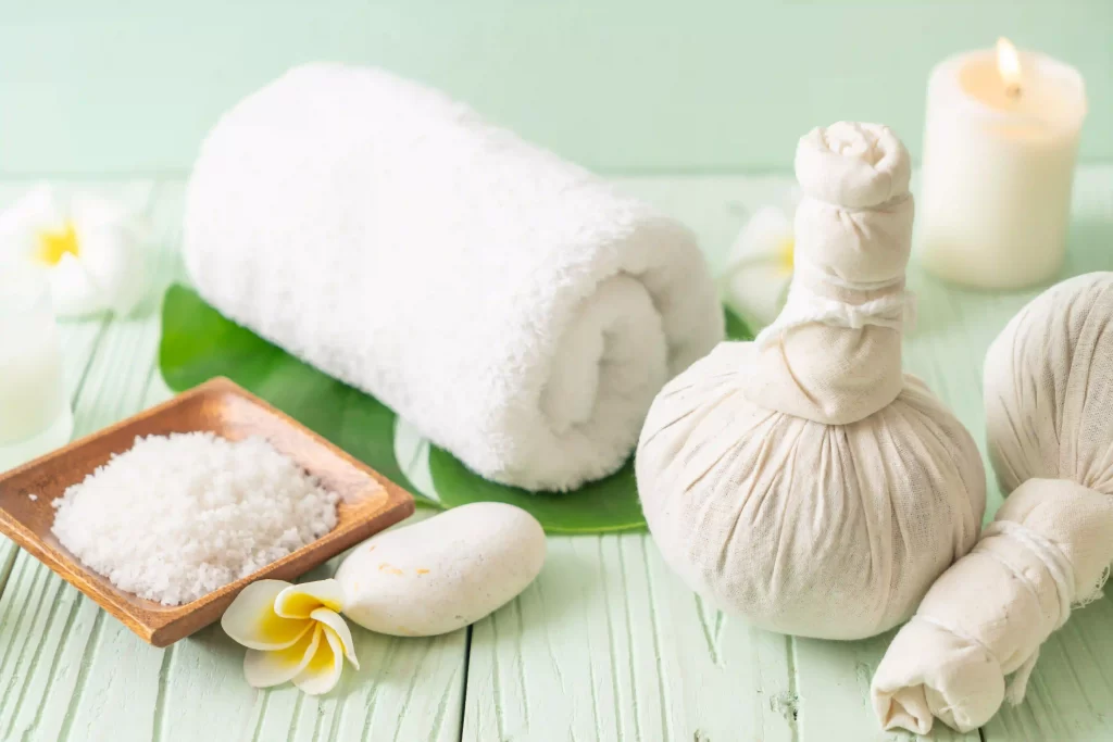 herbal poultice compress balls, rolled towel, candlelight, and frangipani flowers