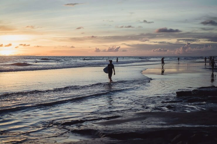Sunset at Seminyak Beach with silhouette of person holding a surfboard