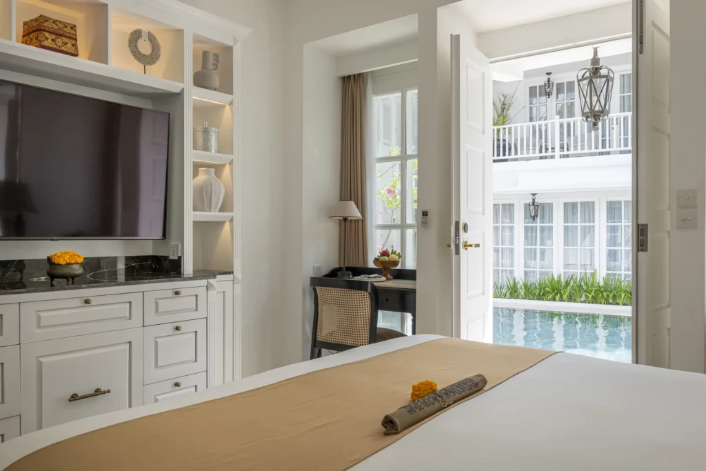 Cozy Deluxe Room featuring bed, work desk, TV, and pool view at boutique accommodation The Colony Hotel Bali, Seminyak.