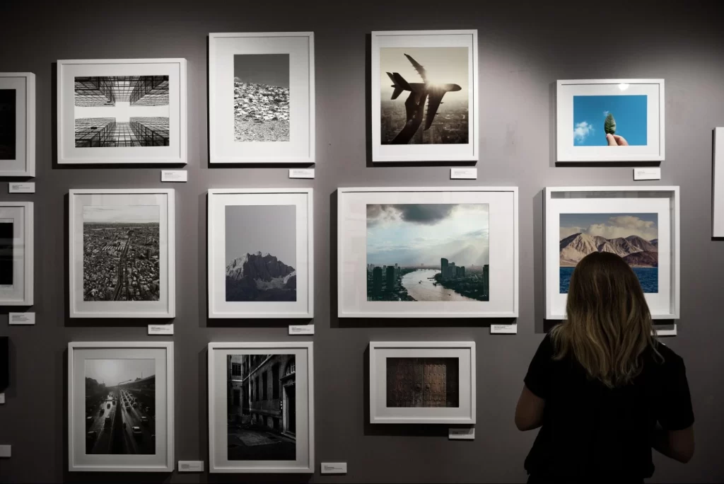 Woman viewing a collection of framed photography prints displayed on a gray gallery wall