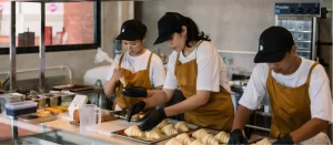 Bakery staff in aprons and caps preparing fresh croissants and pastries