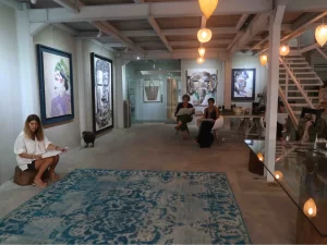 Visitors sitting and browsing artwork in a modern gallery space with large colorful paintings and pendant lights