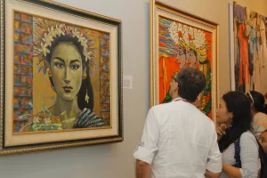 Visitors admiring traditional Balinese portrait paintings with floral headdresses at an art exhibition