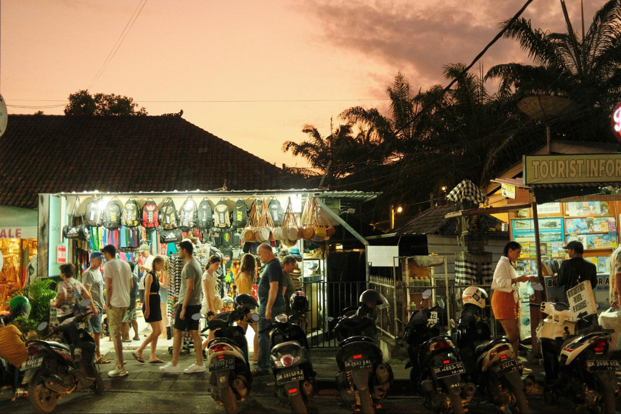 Busy tourist street market at sunset with souvenir shops, scooters, and visitors in Bali nightlife
